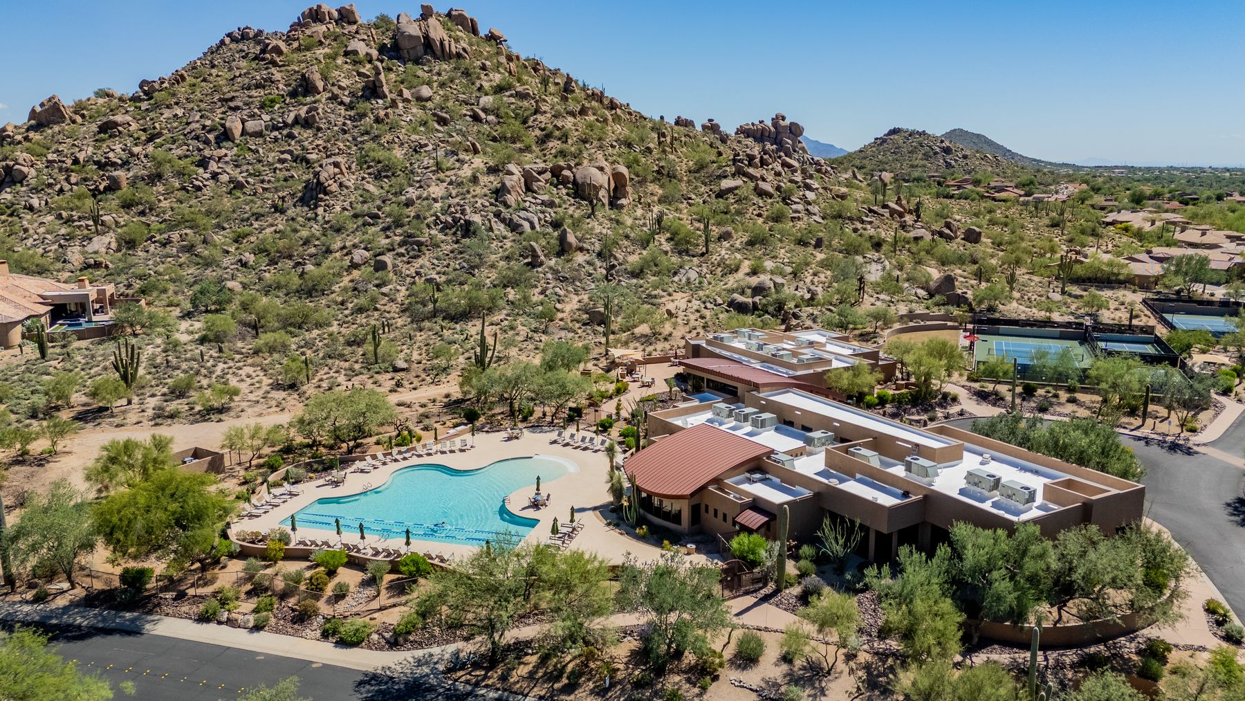 Aerial view of a desert community pool and clubhouse against a boulder hillside