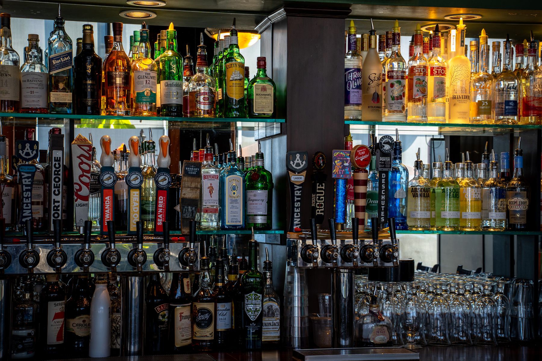 Backlit bar shelving stacked with spirit bottles above a row of draft taps